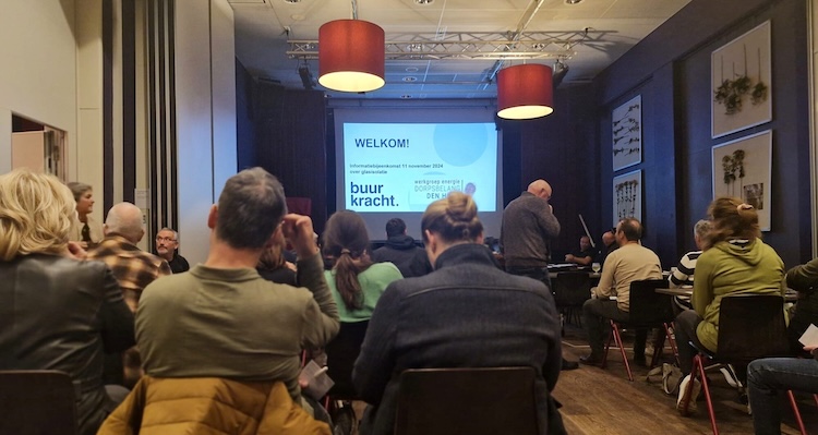 Een groep mensen zit in een ruimte en kijken naar een presentatie op een beamerscherm.