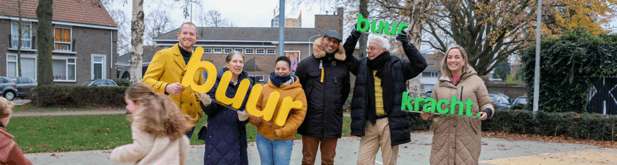 Een groep mensen staat lachend op een basketbalveldje in een woonwijk. Ze hebben Buurkracht letters gemaakt van piepschuim vast en kijken vrolijk naar elkaar en naar de camera. Door het beeld rennen nog twee kinderen.