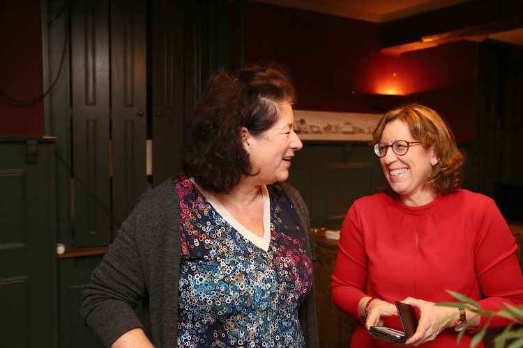 Twee mensen staan in een donkere, gezellige ruimte en kijken lachend naar elkaar.