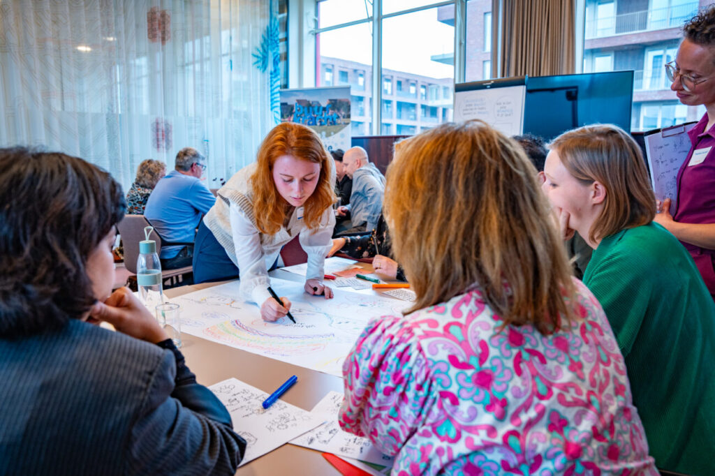 Een groep mensen werkt tijdens een workshop samen aan een tekening bij het Samen sterk met buurkracht evenement