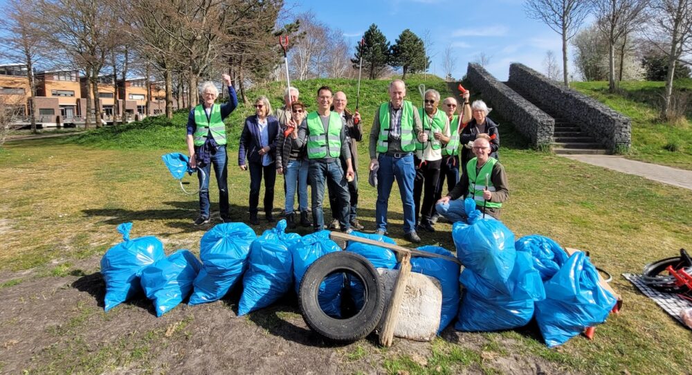 Een groep mensen staat in een parkje voor vuilniszakken met afval dat zij hebben opgeruimd.