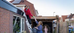 Een persoon staat op een lader en krijgt een spons aangereikt van iemand om het dak schoon te maken.