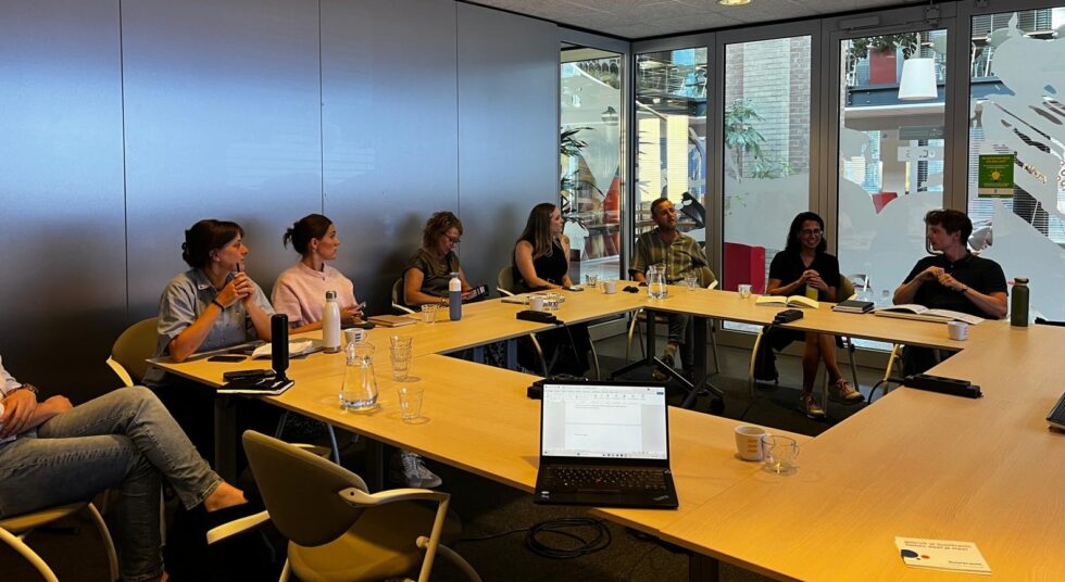 Verschillende ambtenaren zitten met elkaar rond een tafel.