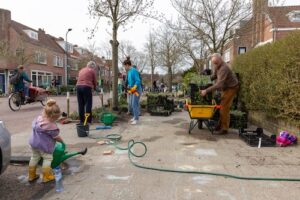 Een groep mensen is in een woonwijk bezig om de boomspiegels te beplanten.